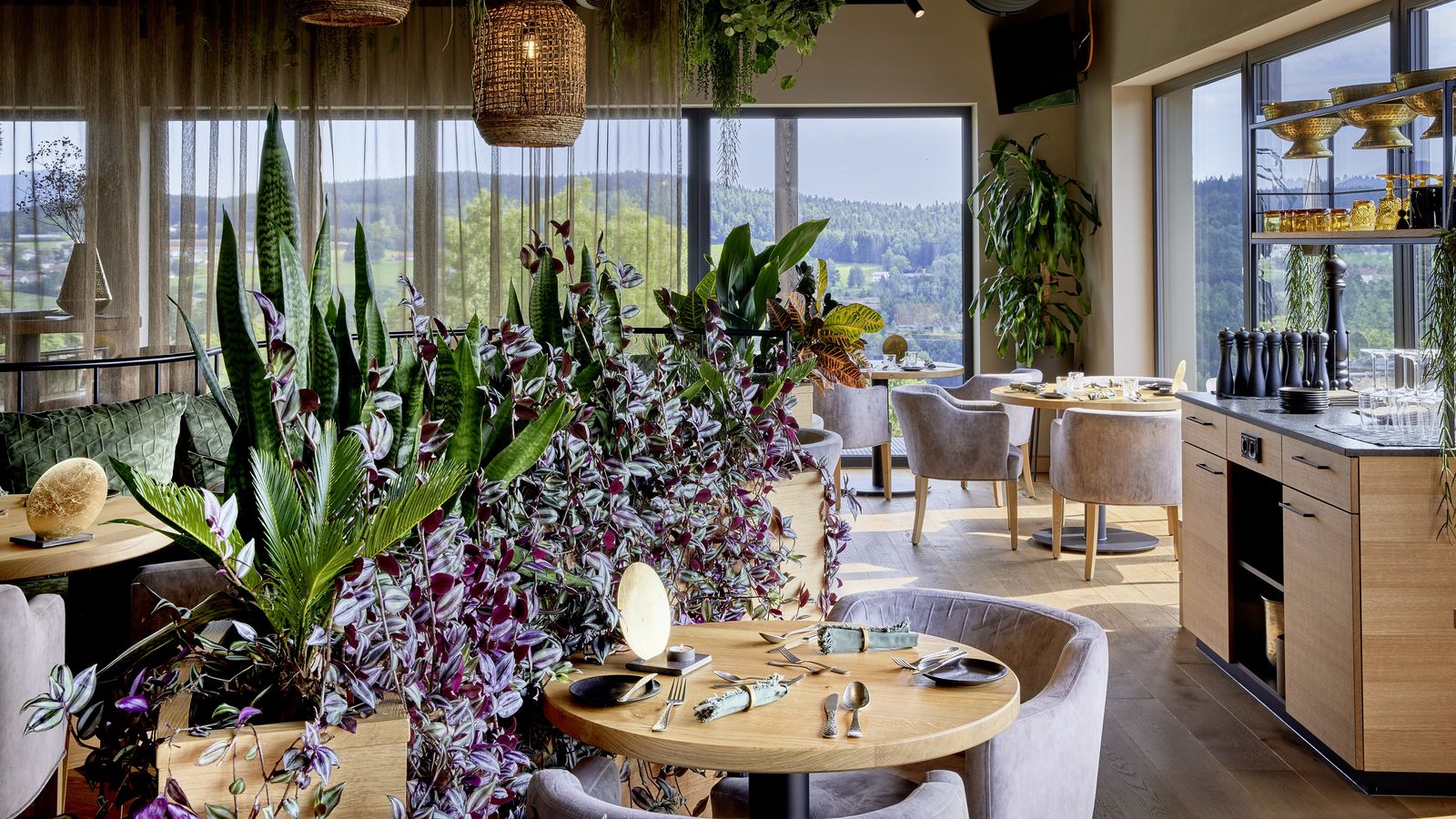 Modernes Panorama-Restaurant „OHM“ im ULRICHSHOF mit stilvoll gedeckten Tischen, üppiger Begrünung, großen Fenstern und Blick auf die Natur des Bayerischen Waldes.