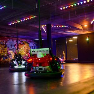Ein Mädchen fährt Autoskooter in der bunt beleuchteten Indoor-Bahn des ULRICHSHOF. Im Hintergrund ist eine farbenfrohe Graffiti-Wand zu sehen.