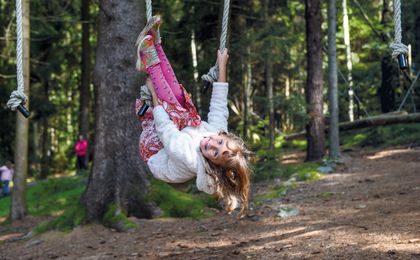 Mädchen klettert im Waldspielplatz an Seilen