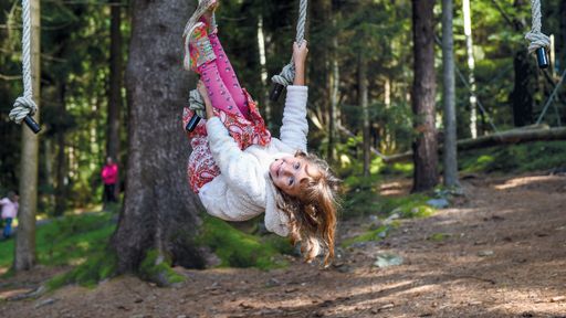 Mädchen klettert im Waldspielplatz an Seilen