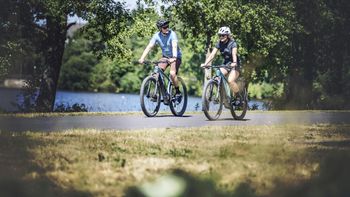 Zwei Menschen radeln mit E-Bikes an einem See im Schwarzwald entlang