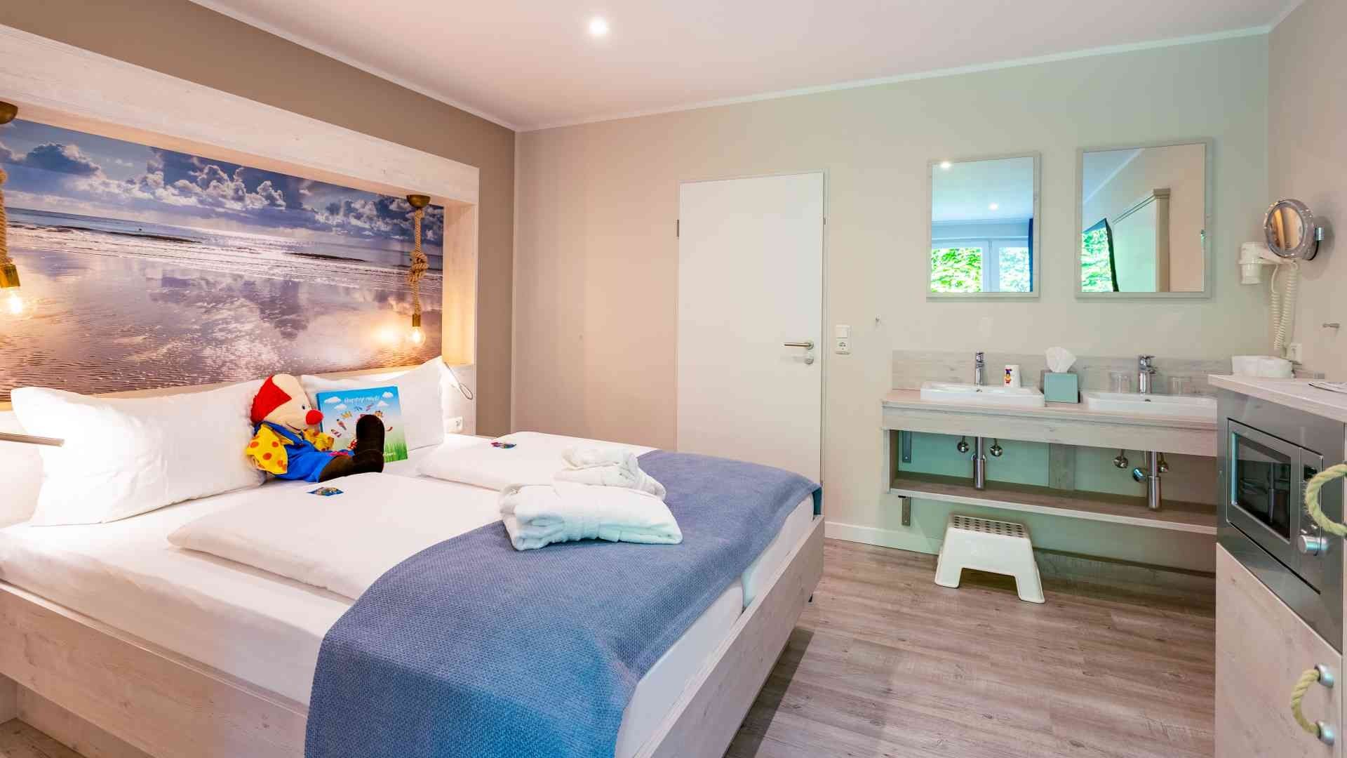 Blick auf das Doppelbett, den Doppelwaschtisch im Zimmer und die Mikrowelle in der Familien-Suite Typ A