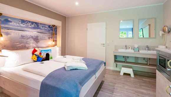 Blick auf das Doppelbett, den Doppelwaschtisch im Zimmer und die Mikrowelle in der Familien-Suite Typ A