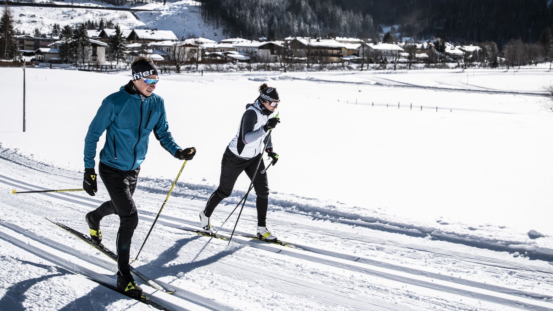 Zwei Personen beim Langlaufen in Gastein vor verschneiter Bergkulisse – Winterurlaub nahe Hotel Sonngastein.