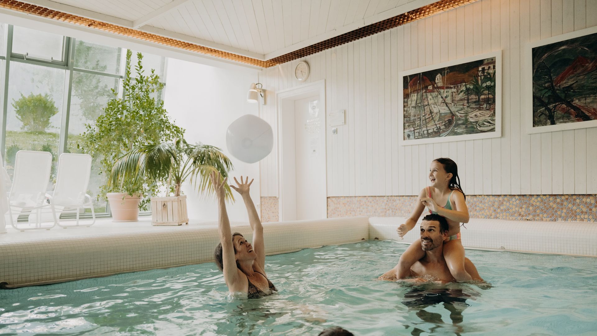 Familie spielt im hellen Hotelpool mit Ball und entspannt im Wasser