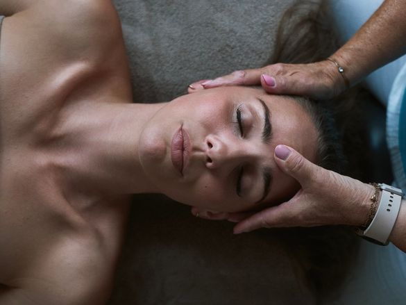 Frau bei einer Kopfmassage liegt mit geschlossenen Augen auf der Massageliege
