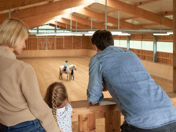 Tochter beim Reiten in der Reithalle des Schreinerhofs während Eltern und Schwester zuschauen