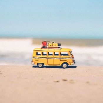 Ein gelber Spielzeug-Campingbus steht auf dem Strand und symbolsiert die nachhaltige Anreise in den Urlaub