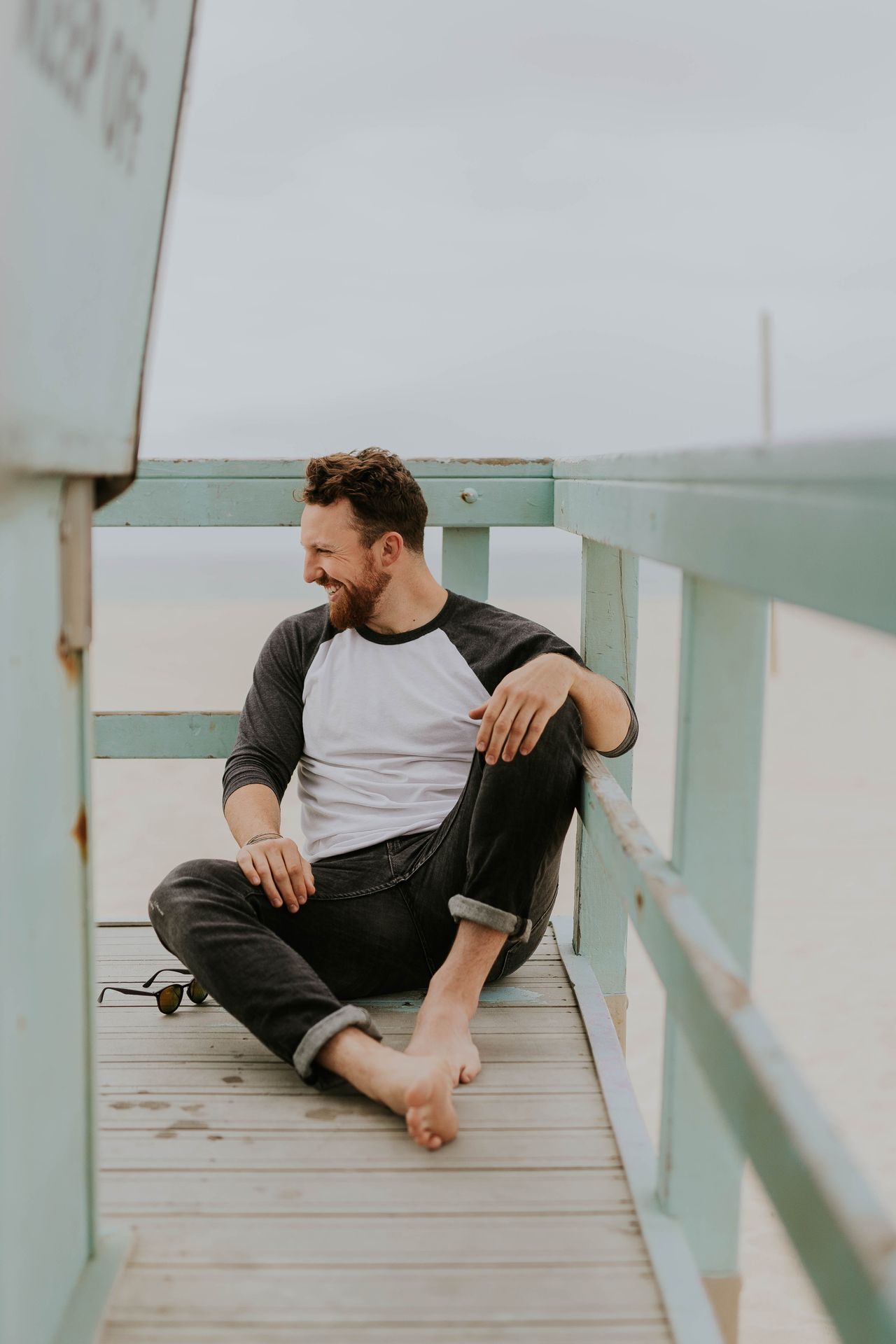 Ein junger Mann sitzt, im Rahmen seines Urlaubs an der Ostsee, alleine an ein weißes Geländer angelehnt und lächelt breit