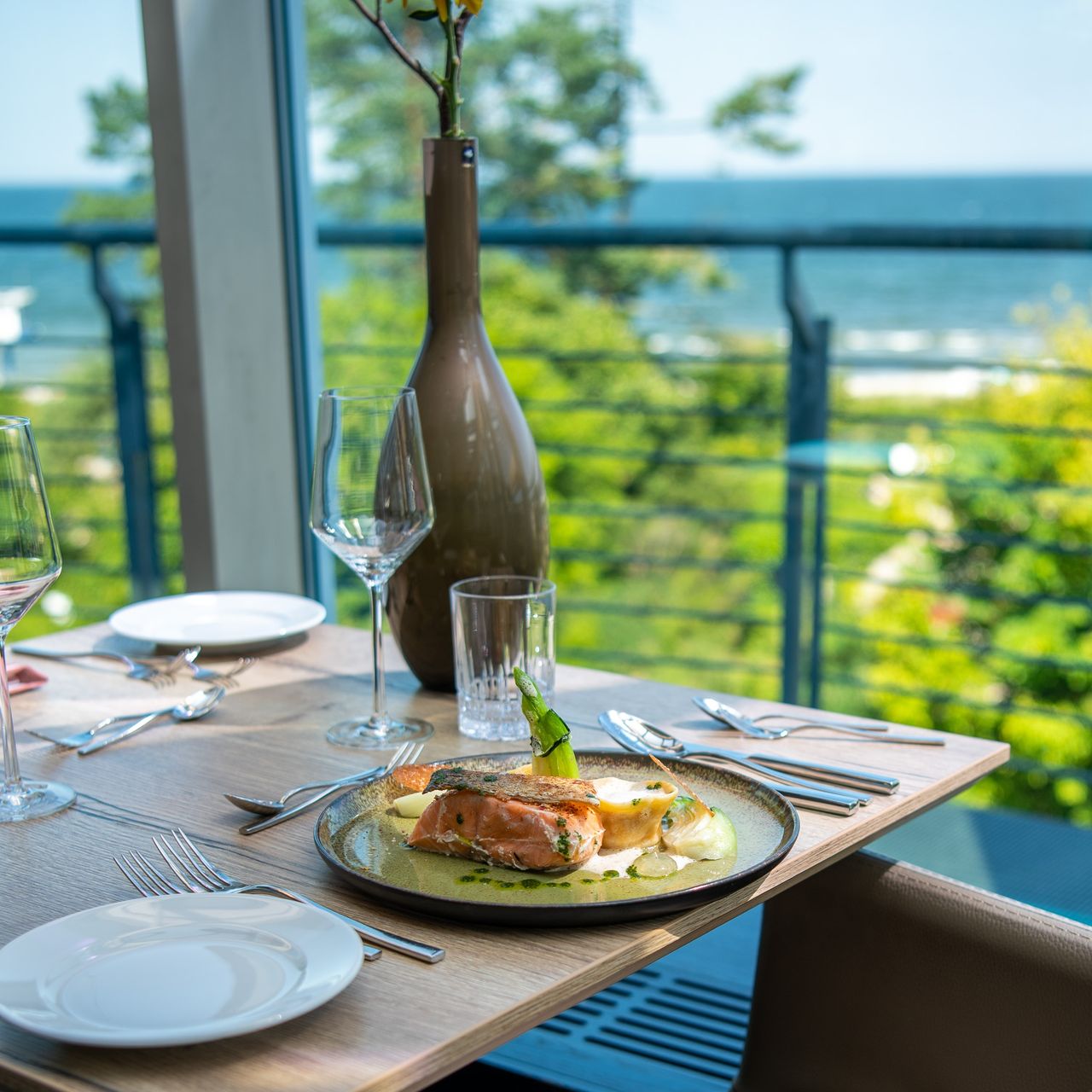 Ein Teller mit einem Fisch Hauptgang steht auf einem gedeckten Tisch am Fenster eines Panoramarestaurants mit Blick auf die Ostsee