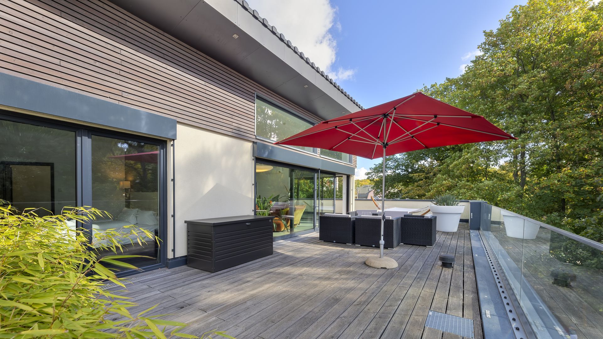 Dachterrasse der Penthouse-Wohnung mit Sonnenschirm und Blick in die Bäume