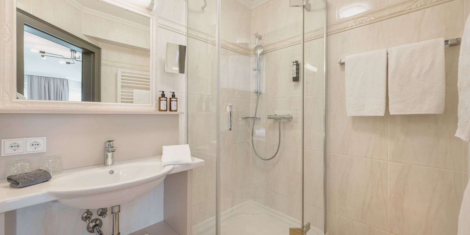 Modernes Badezimmer mit Dusche im Hotel die HOCHKÖNIGIN in Maria Alm, mit hellen Fliesen, hochwertigen Details und Pflegeprodukten.