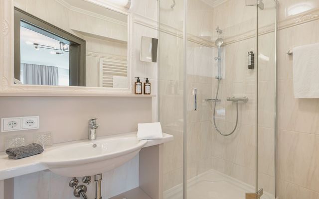 Modernes Badezimmer mit Dusche im Hotel die HOCHKÖNIGIN in Maria Alm, mit hellen Fliesen, hochwertigen Details und Pflegeprodukten.
