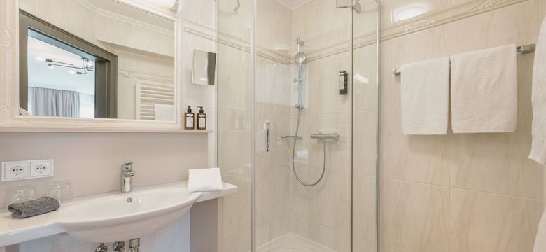 Modernes Badezimmer mit Dusche im Hotel die HOCHKÖNIGIN in Maria Alm, mit hellen Fliesen, hochwertigen Details und Pflegeprodukten.