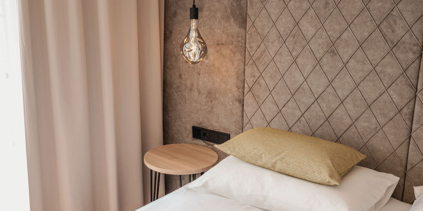 Ein stilvolles Schlafzimmer-Detail im Hotel die HOCHKÖNIGIN in Maria Alm: edles Kopfteil mit Steppmuster, sanfte Stoffe, natürliche Farben und eine Designerleuchte, die Gemütlichkeit mit modernem Stil verbindet.