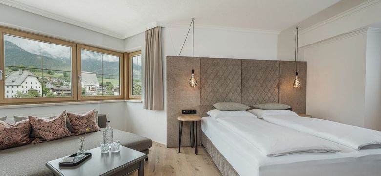 Modernes Zimmer im Hotel die HOCHKÖNIGIN in Maria Alm mit Blick auf das Dorf und die Berge, stilvollem Interieur und edlen Details.