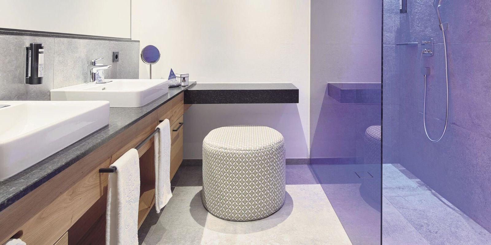 Edles, modernes Badezimmer im Hotel die HOCHKÖNIGIN in Maria Alm: großzügiges Doppelwaschbecken, stilvolle Walk-in-Dusche mit Glasfront, hochwertiger Kosmetikbereich und helle, zeitlose Materialien. Perfekt für Gäste, die Komfort, Design und viel Platz schätzen.