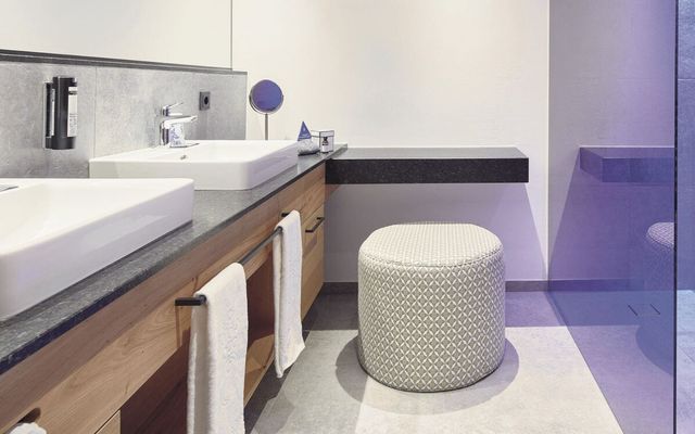 Edles, modernes Badezimmer im Hotel die HOCHKÖNIGIN in Maria Alm: großzügiges Doppelwaschbecken, stilvolle Walk-in-Dusche mit Glasfront, hochwertiger Kosmetikbereich und helle, zeitlose Materialien. Perfekt für Gäste, die Komfort, Design und viel Platz schätzen.