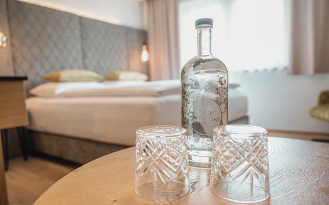 Zimmer im Hotel die HOCHKÖNIGIN mit Blick auf das Bett und Wasserflsche mit Kristallgläsern am Tisch