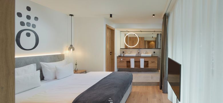 Zimmer im Hotel die HOCHKÖNIGIN mit Blick auf das Bett und ins Zimmer hinein zum offenen Badezimmer mit Doppelwaschbecken
